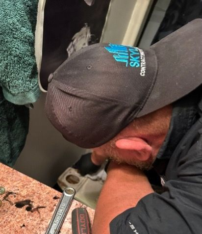 Person wearing a cap works on plumbing under a sink, holding tools, close-up shot.