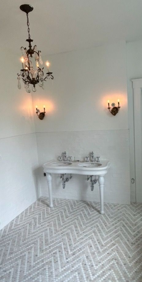 Elegant bathroom with chandelier, sconces, and double sink on herringbone tile floor.