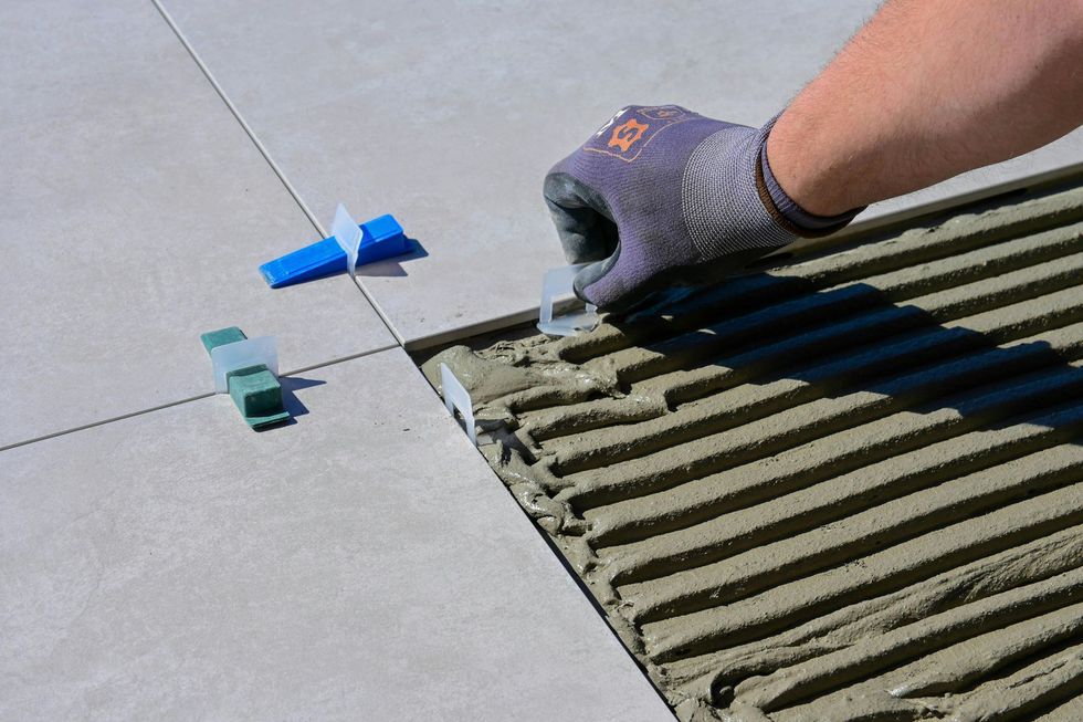 Person in glove using tile leveling system on floor with fresh mortar.