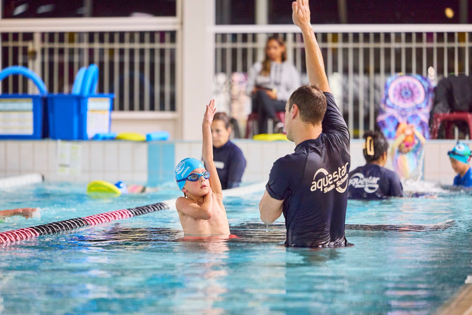 Child in swim class raises arm, instructor assists in a pool.