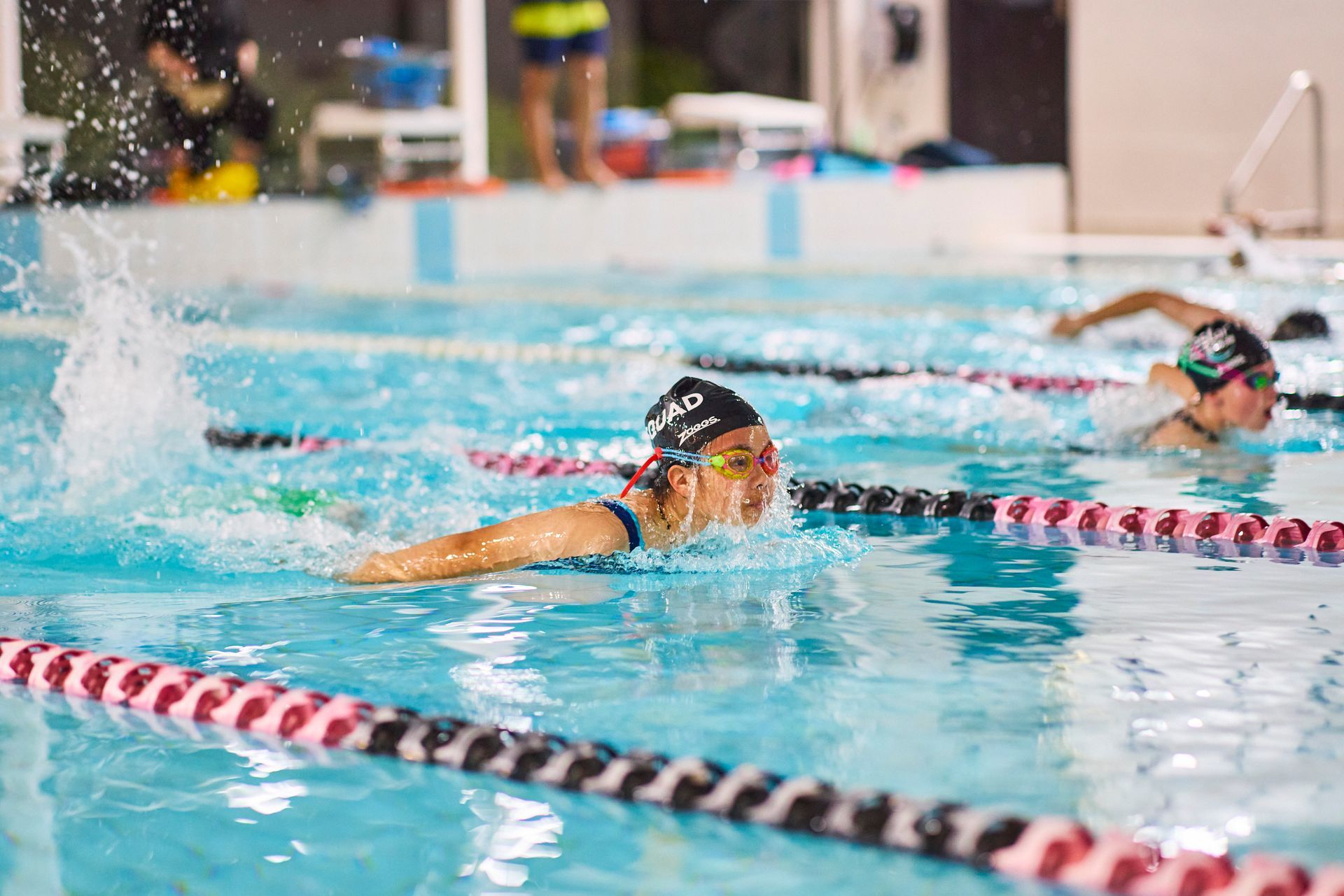 Boy in pool with instructor; boy smiles, reaching for toy. Indoor pool setting.