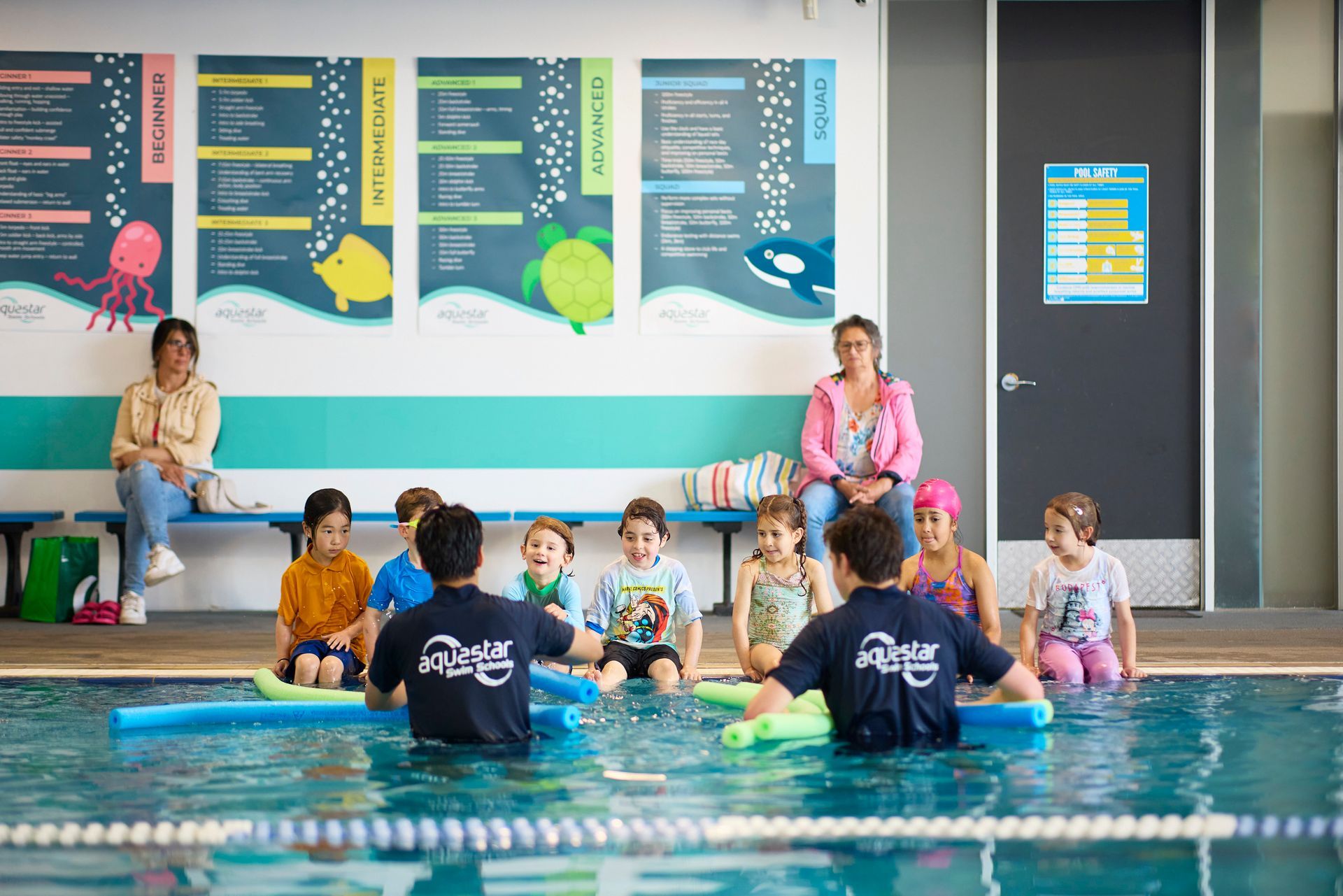 Girl in a pink swim cap and goggles swimming backstroke in a pool.