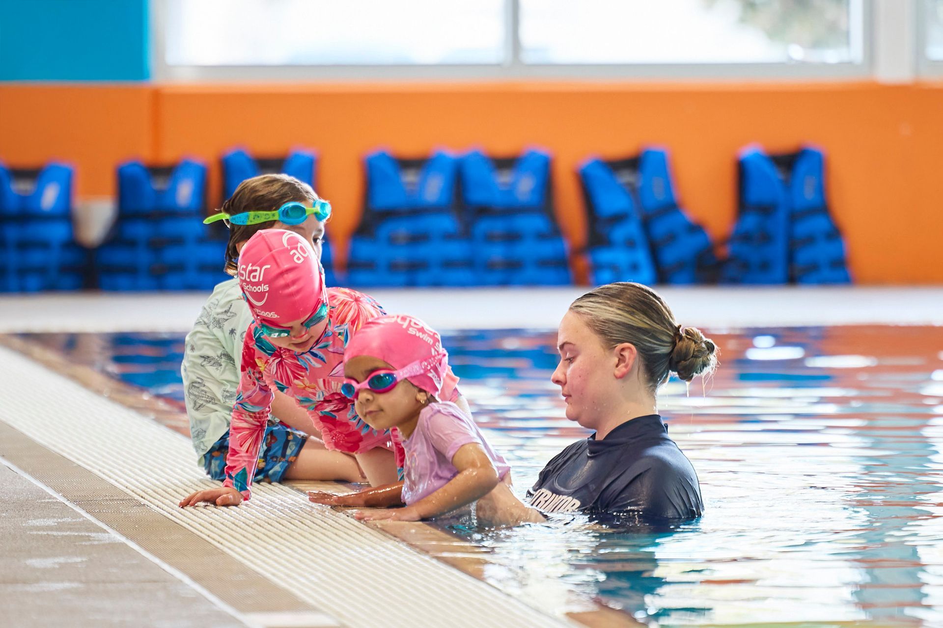 A swim teacher is helping 3 young swimmers safely climb out of the pool