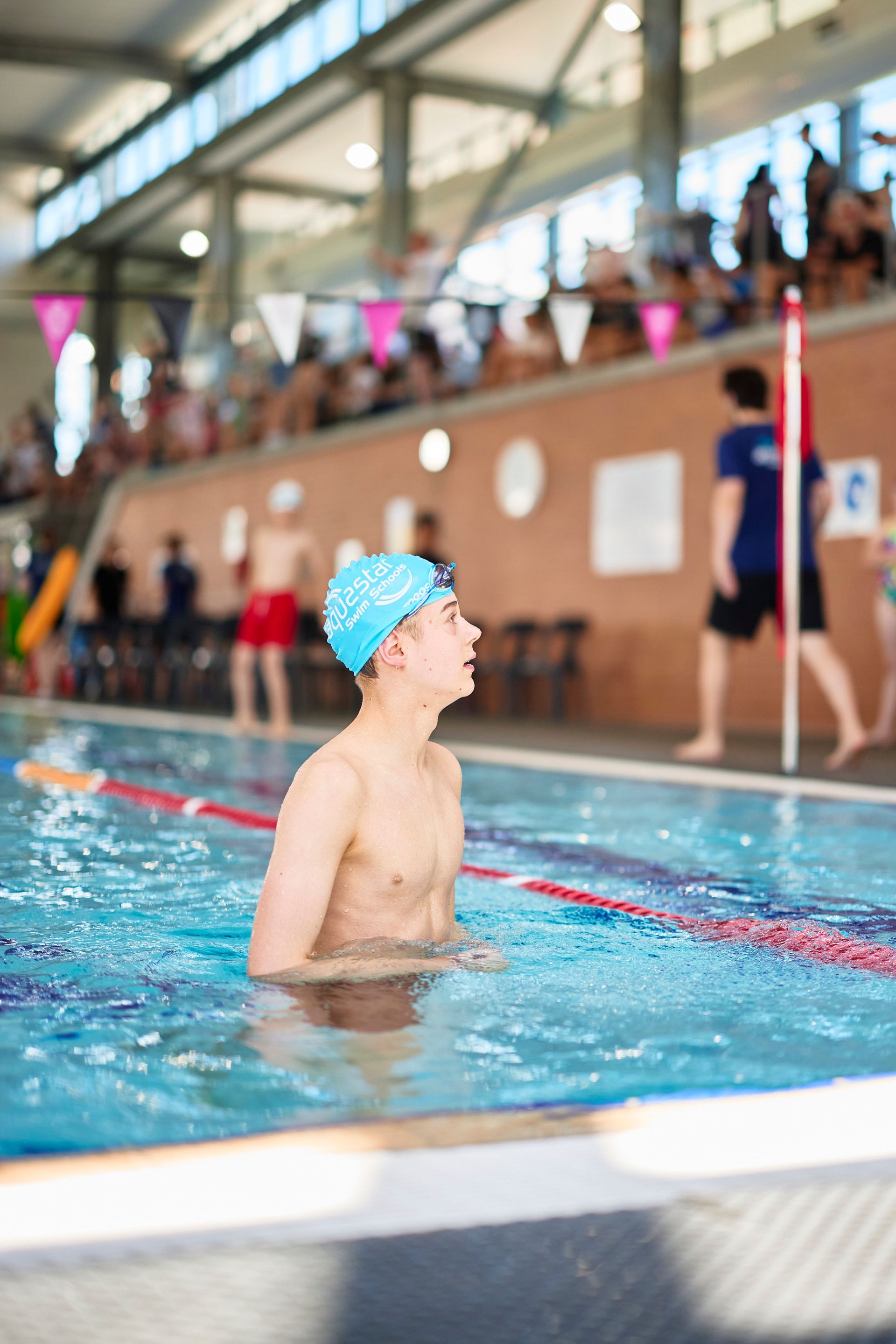 Swimmer in blue cap looking up in pool at a swim meet.
