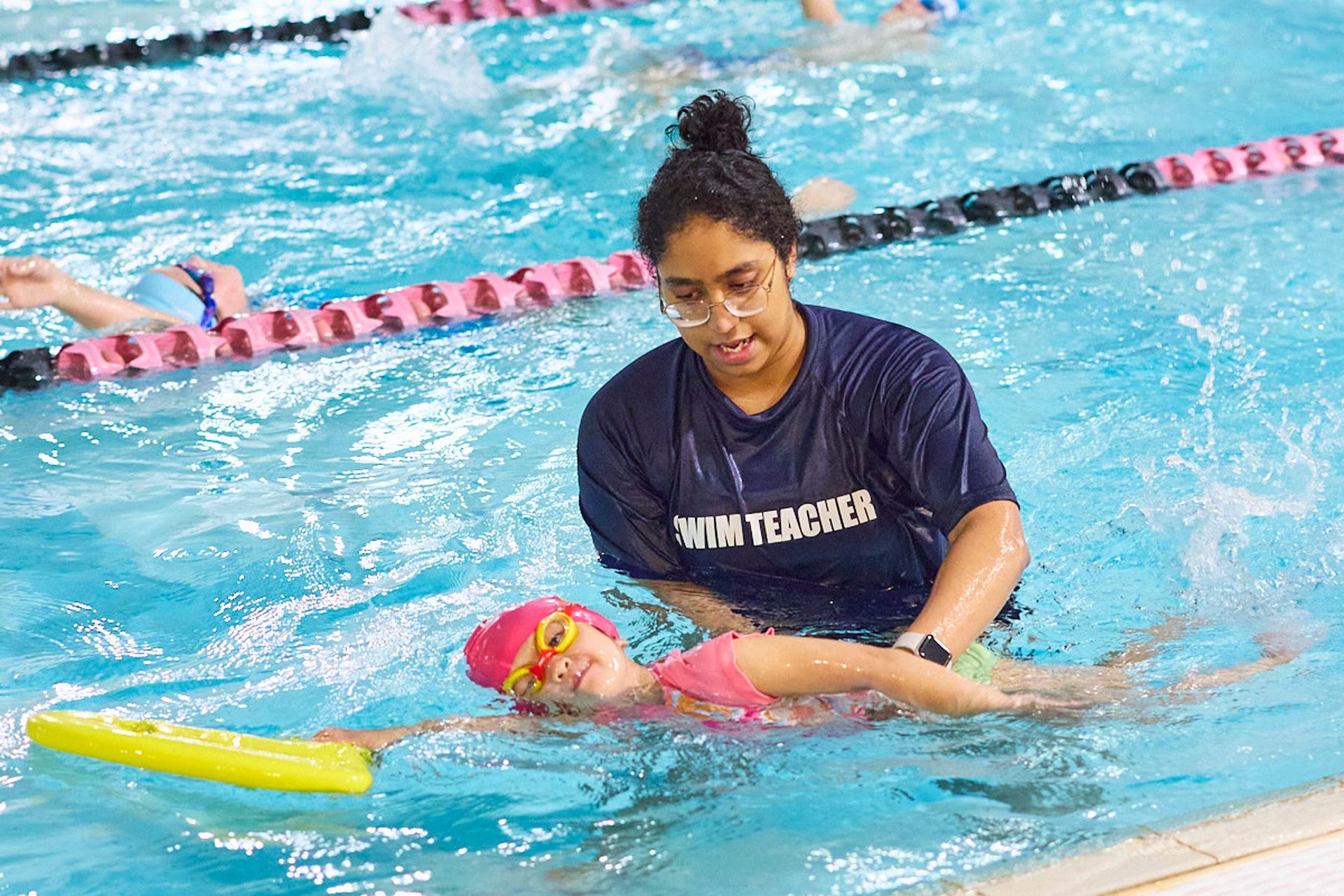 Swim teacher helps a child in pink cap learn to swim in pool.