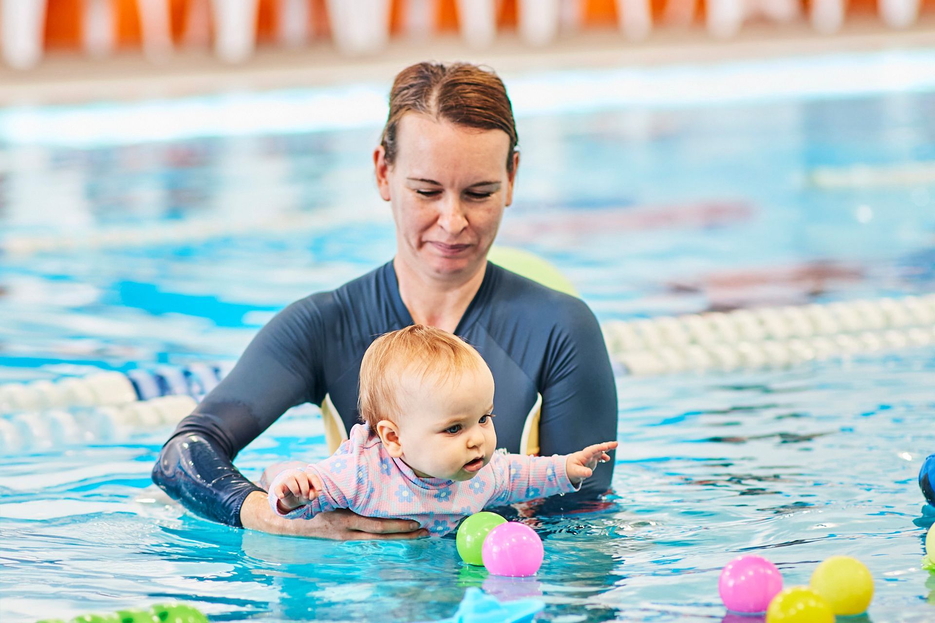 Woman teaching baby to swim in a pool, holding the baby in the water.