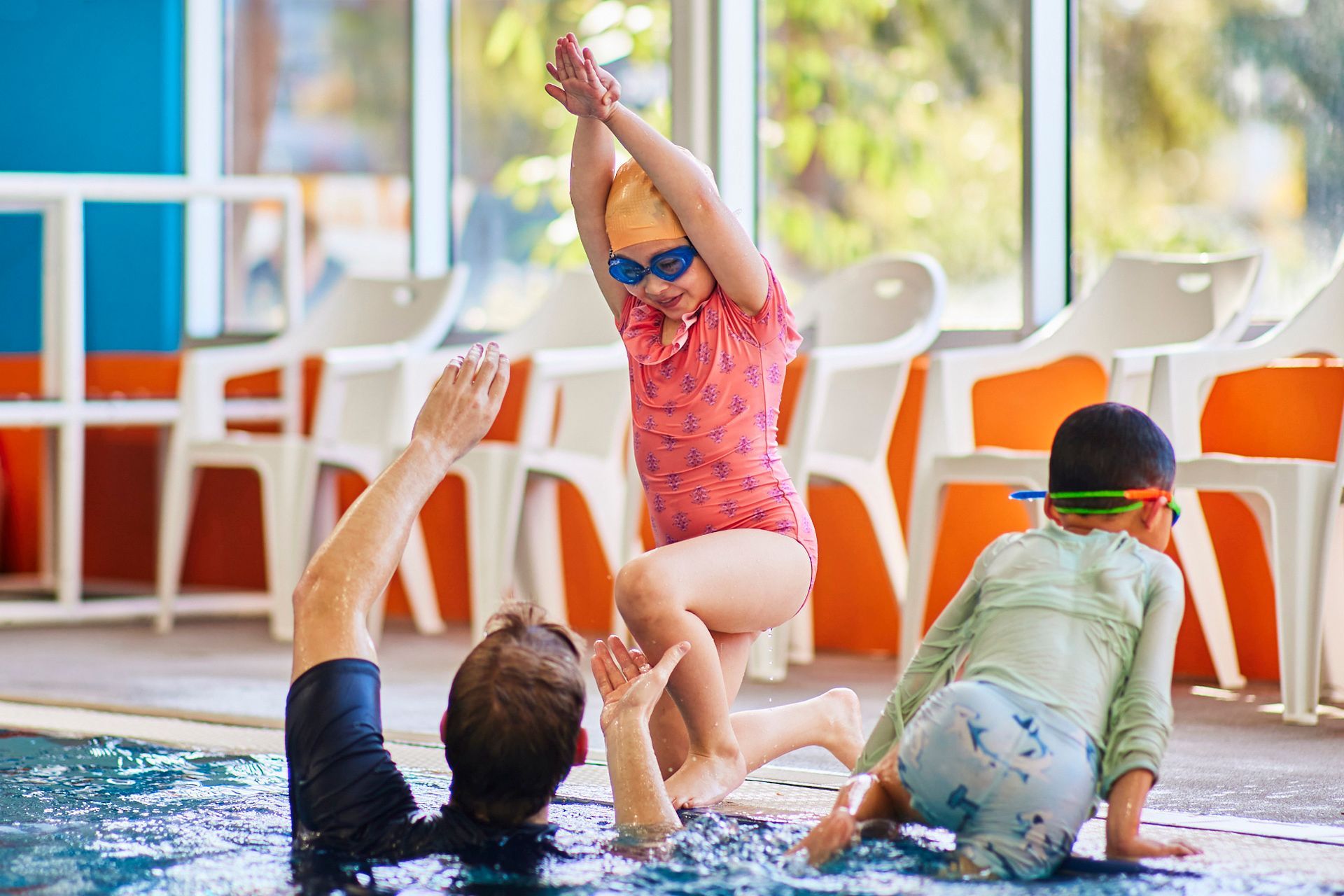 Young girl doing kneeling dive into the deep end of the pool. Assisted by a swim teacher.