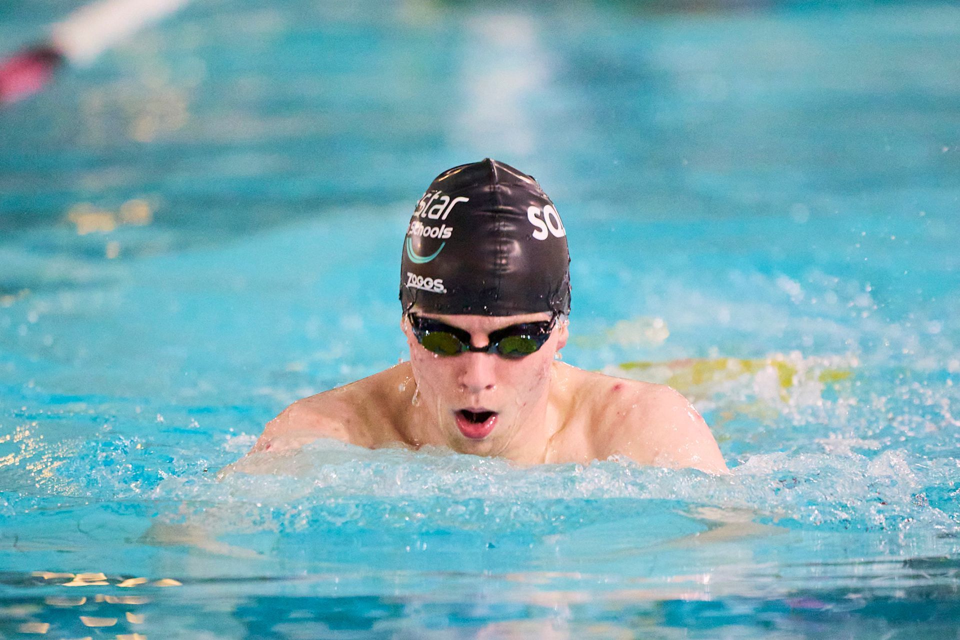 Swimmer in a pool wearing goggles and a swim cap, performing the breaststroke.