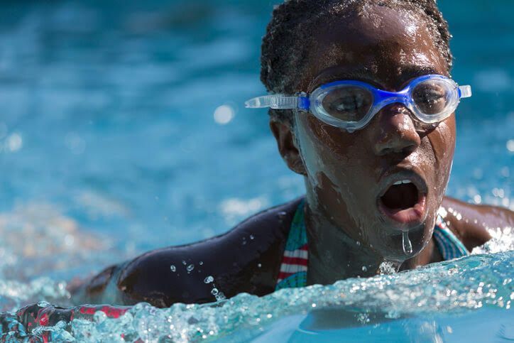 Swimmer in blue goggles, face out of water, mouth open, swimming in a pool.