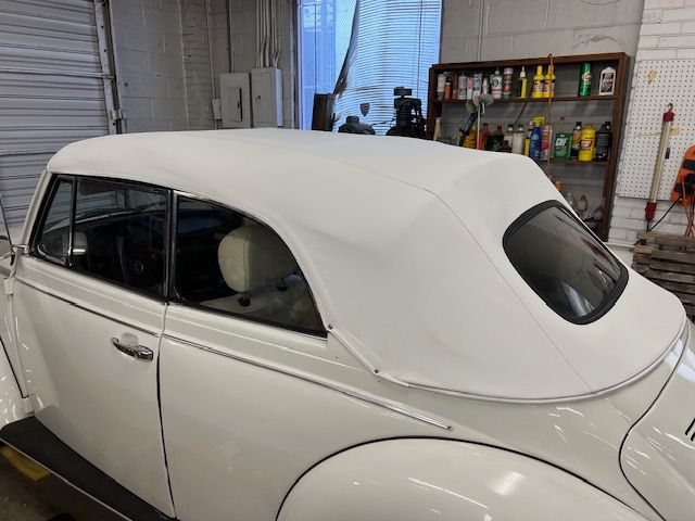 White convertible Beetle with a new white soft top, parked indoors.