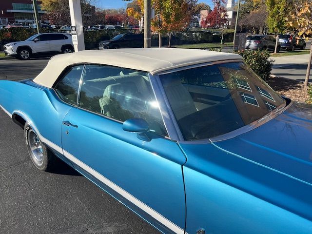 Blue convertible car with white top, parked on a street.
