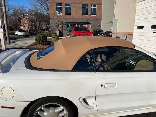White Ford Mustang convertible with tan top parked on a sunny day.