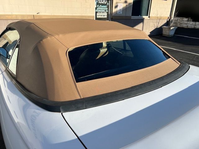 White convertible car with a tan soft top, black window, and a shadow cast on the vehicle.