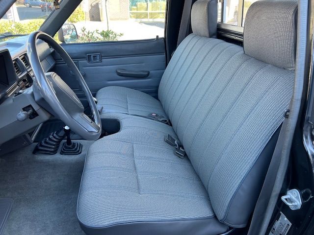 Interior of a vintage black pickup truck with grey bench seat, steering wheel, and gear shift.