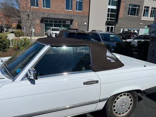 White Mercedes convertible with brown top, parked outside a building on a sunny day.
