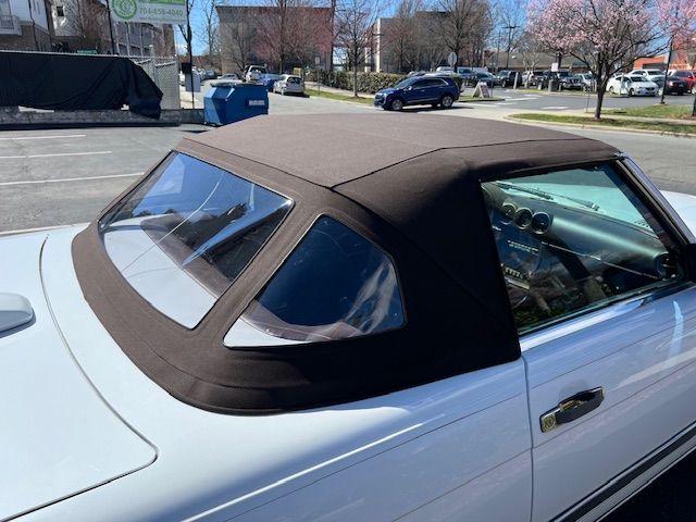 White convertible car with a dark brown fabric top in a street setting.