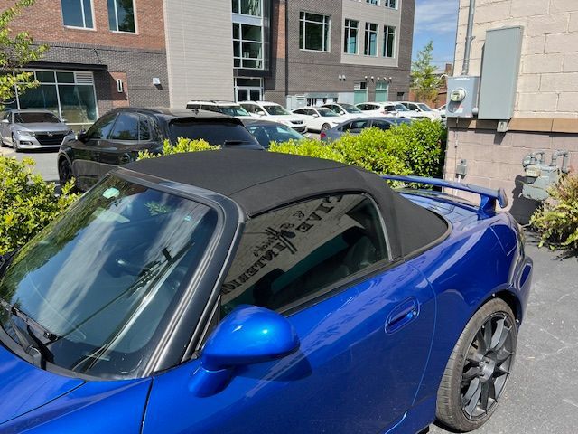 Blue convertible sports car with black top parked outdoors near a building and other vehicles.