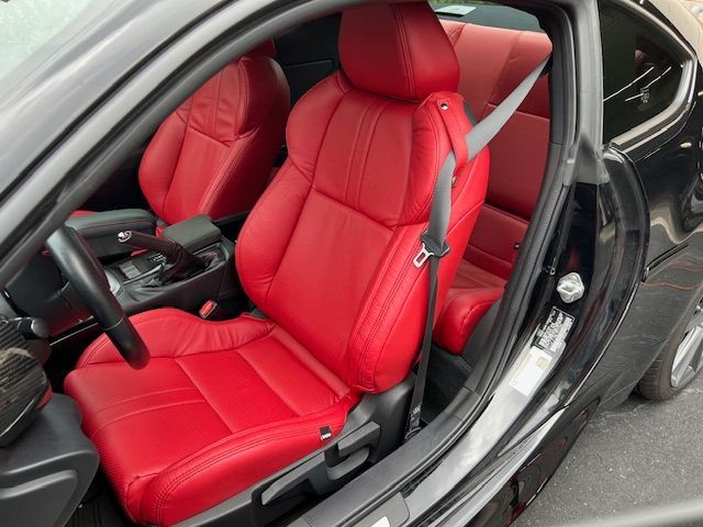 Red leather car seats in a black vehicle with the driver's side door open.