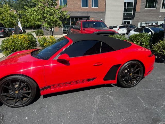 Red Porsche convertible with black roof and wheels parked outside.