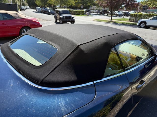 Blue convertible car with black soft top, parked on a street on a sunny day.