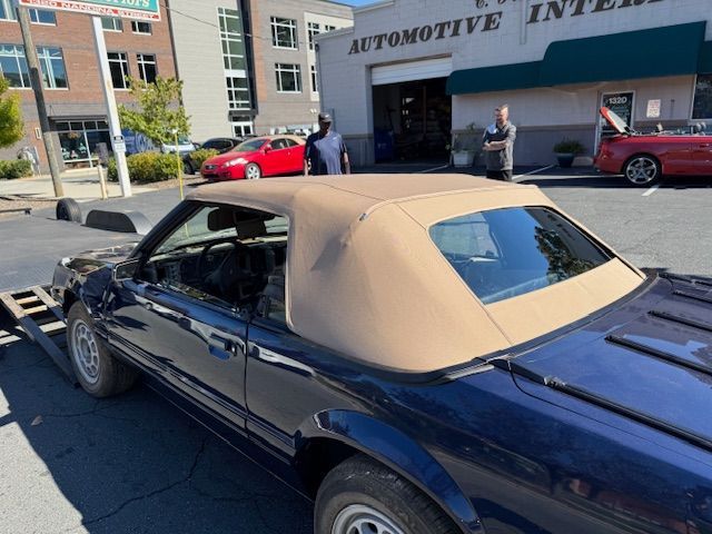 Dark blue Ford Mustang convertible with tan top, parked in front of an auto repair shop.