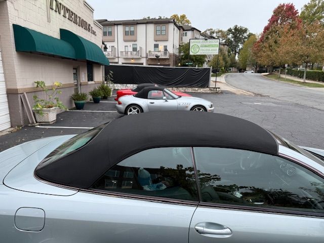 Silver convertible car parked in front of a building with a green awning. Another convertible parked behind.