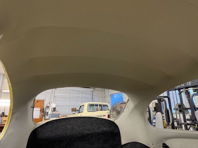 Interior of a vehicle with a cream-colored headliner and windows overlooking a workshop.