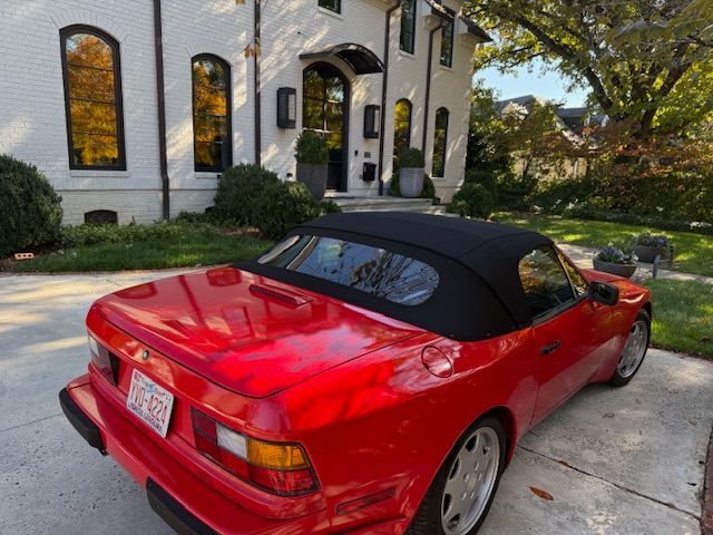 Red Porsche convertible parked in front of a white house with black trim. Black convertible top is up.
