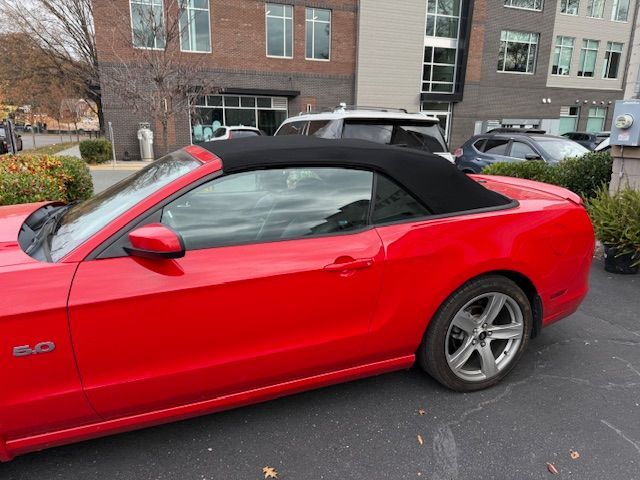 Red convertible Mustang with black top parked outdoors.