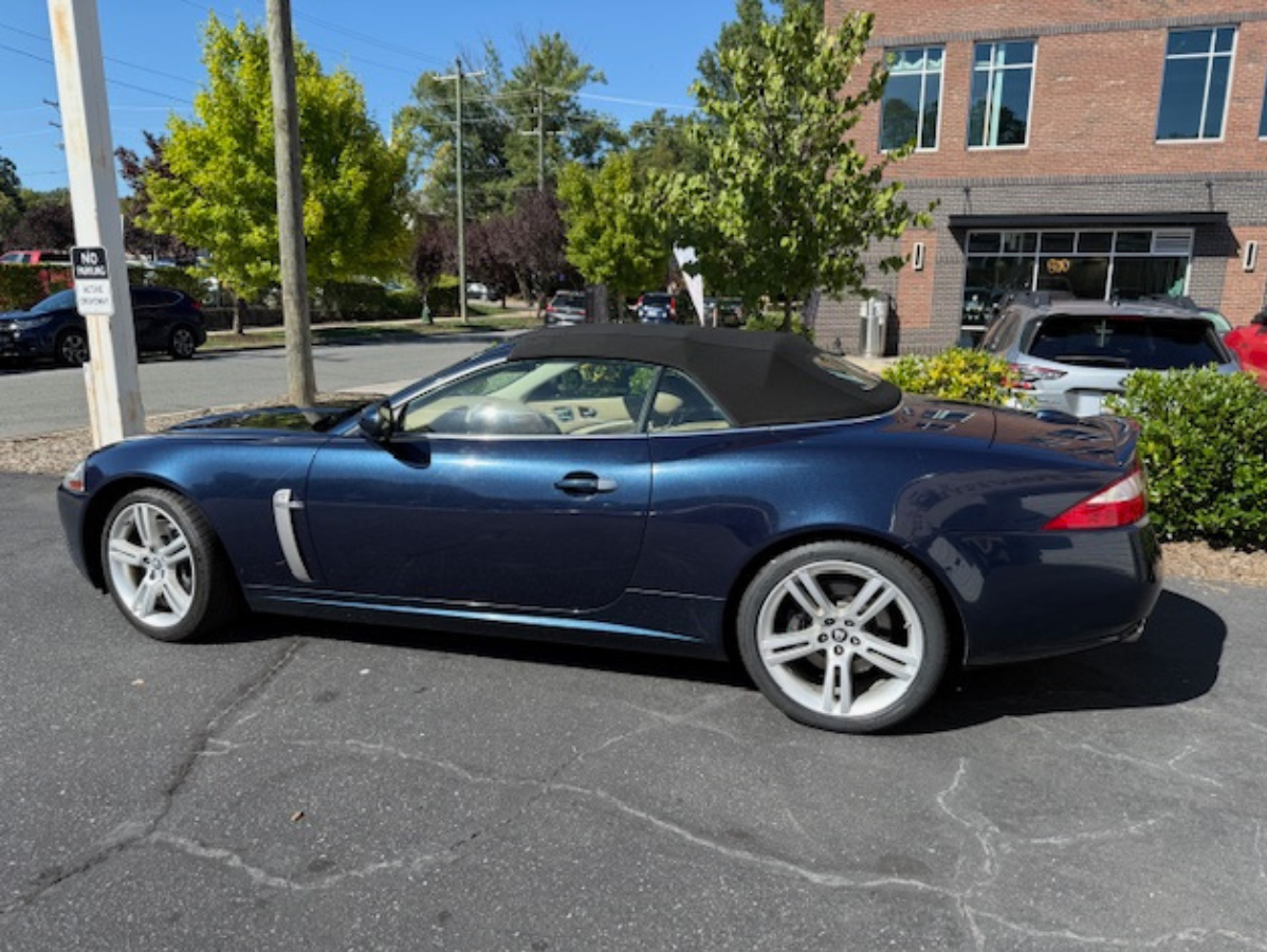 Blue Jaguar convertible parked outside a brick building on a sunny day.