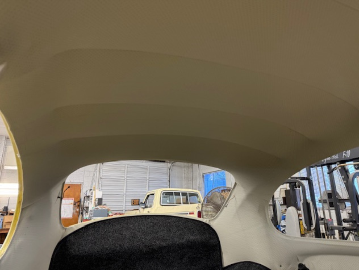 Interior view of a vehicle; cream-colored headliner, rear window frames a yellow pickup truck in a shop.