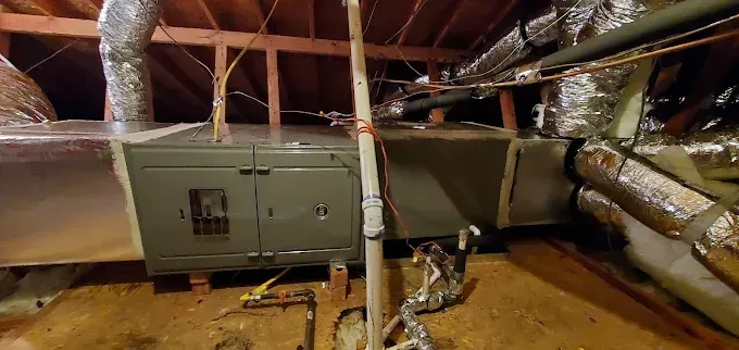 HVAC unit in an attic with insulated ducts and exposed ceiling beams