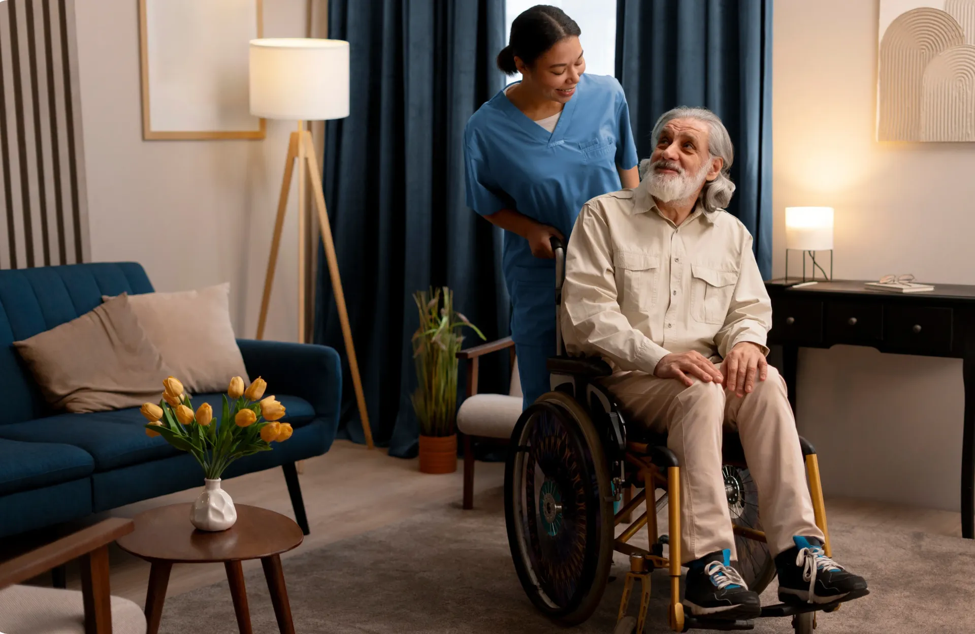 An elderly man in a wheelchair is being helped by a nurse in a living room.