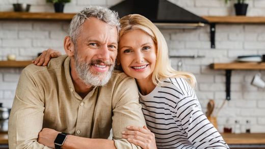 A man and a woman are posing for a picture in a kitchen.