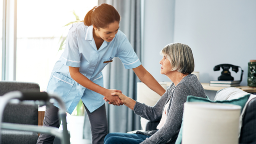 A nurse is shaking hands with an elderly woman in a living room.