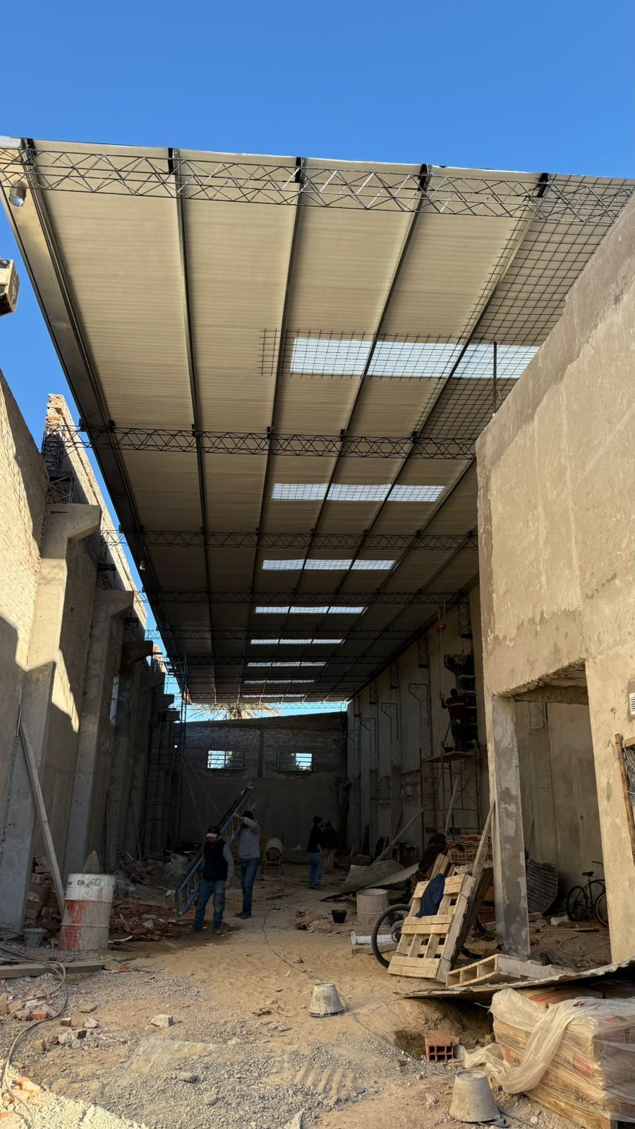 Vista interior de un edificio ruinoso con el tejado parcialmente derrumbado. Dos personas caminan hacia la luz del sol que se filtra por las aberturas.