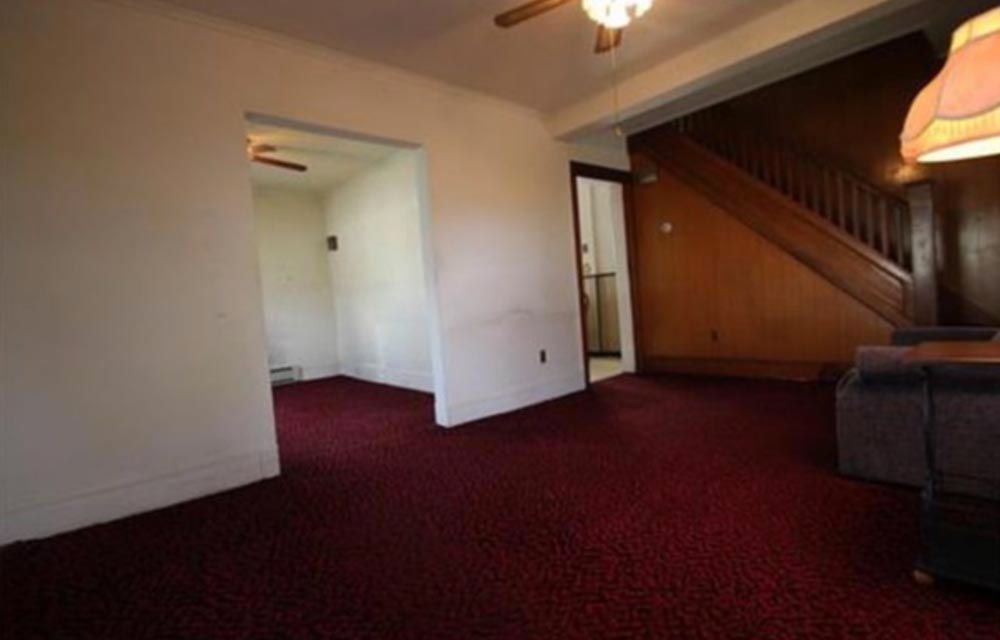 Pre-renovation home interior with red carpet and wood-paneled staircase