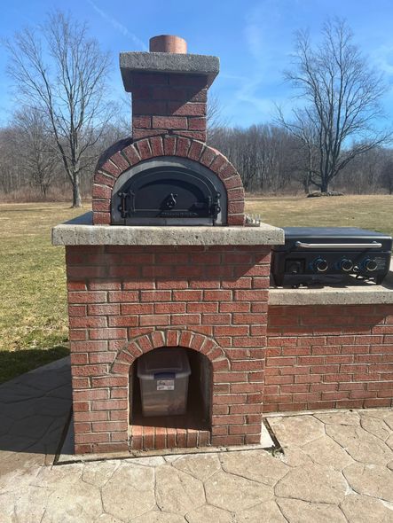 Brick outdoor oven with chimney and adjacent grill on a patio.