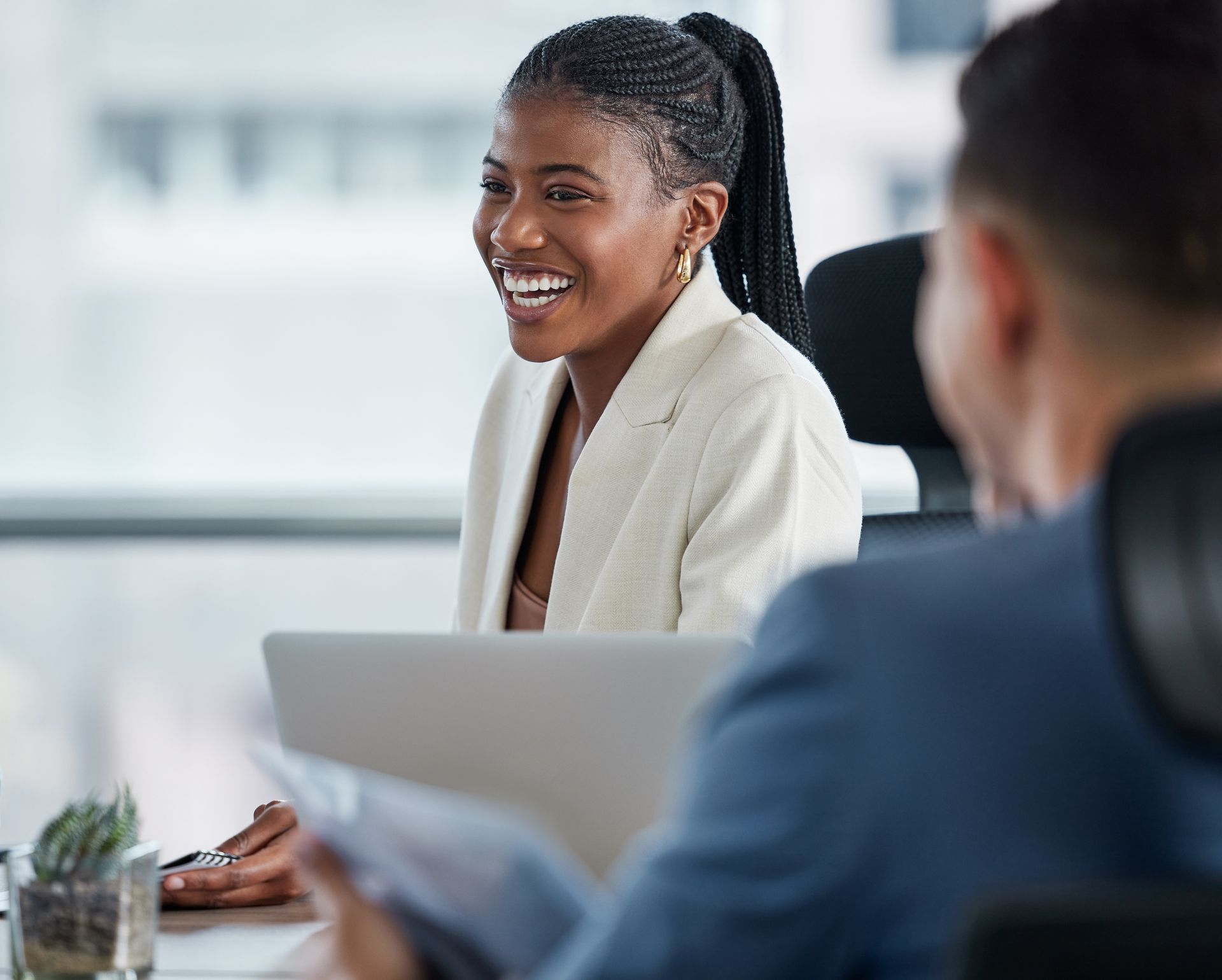 A woman is smiling while sitting at a desk with a laptop