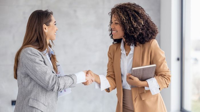 Two women are shaking hands in an office.