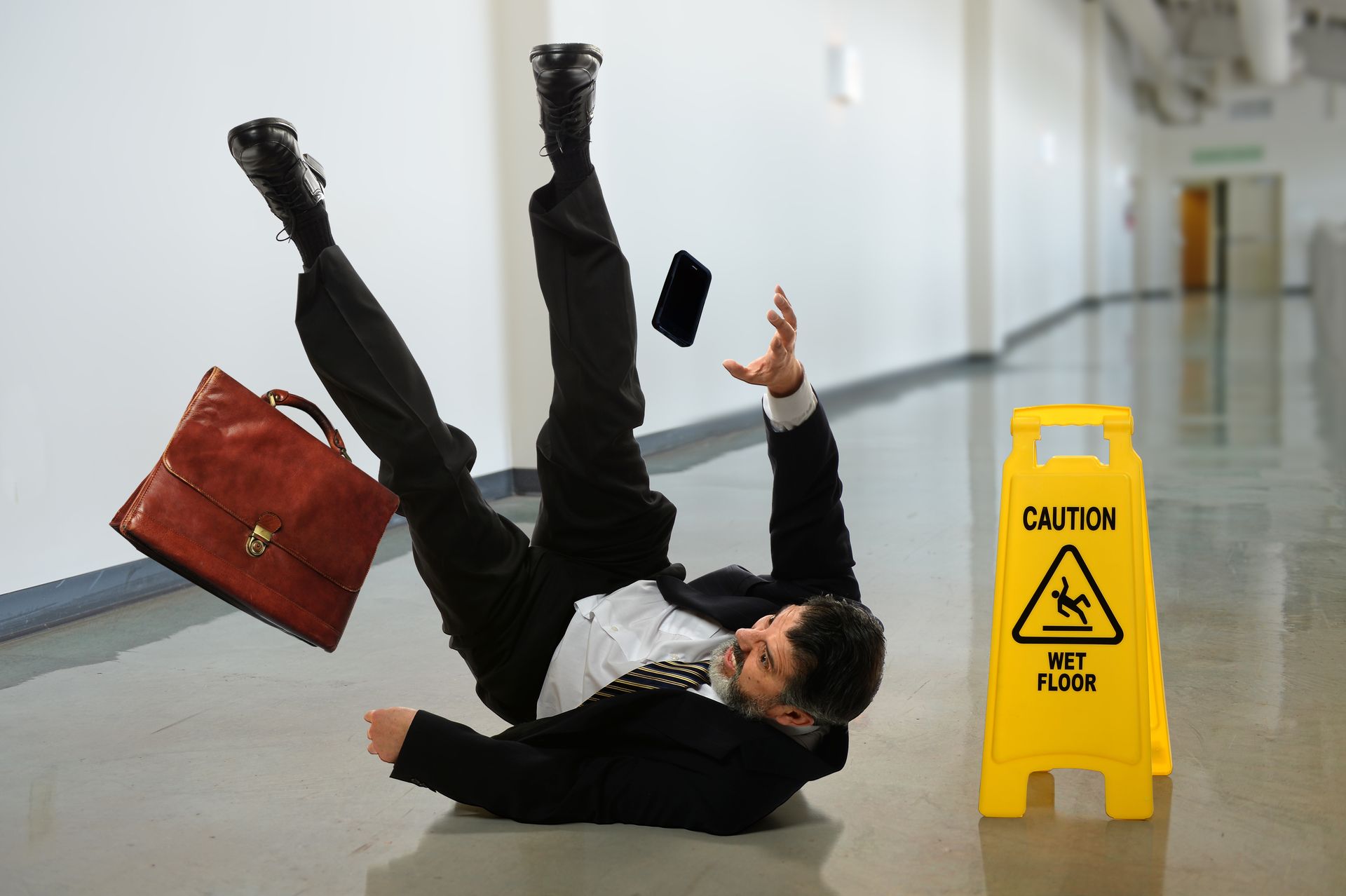 A businessperson slipping on a wet floor in a hallway with a caution sign