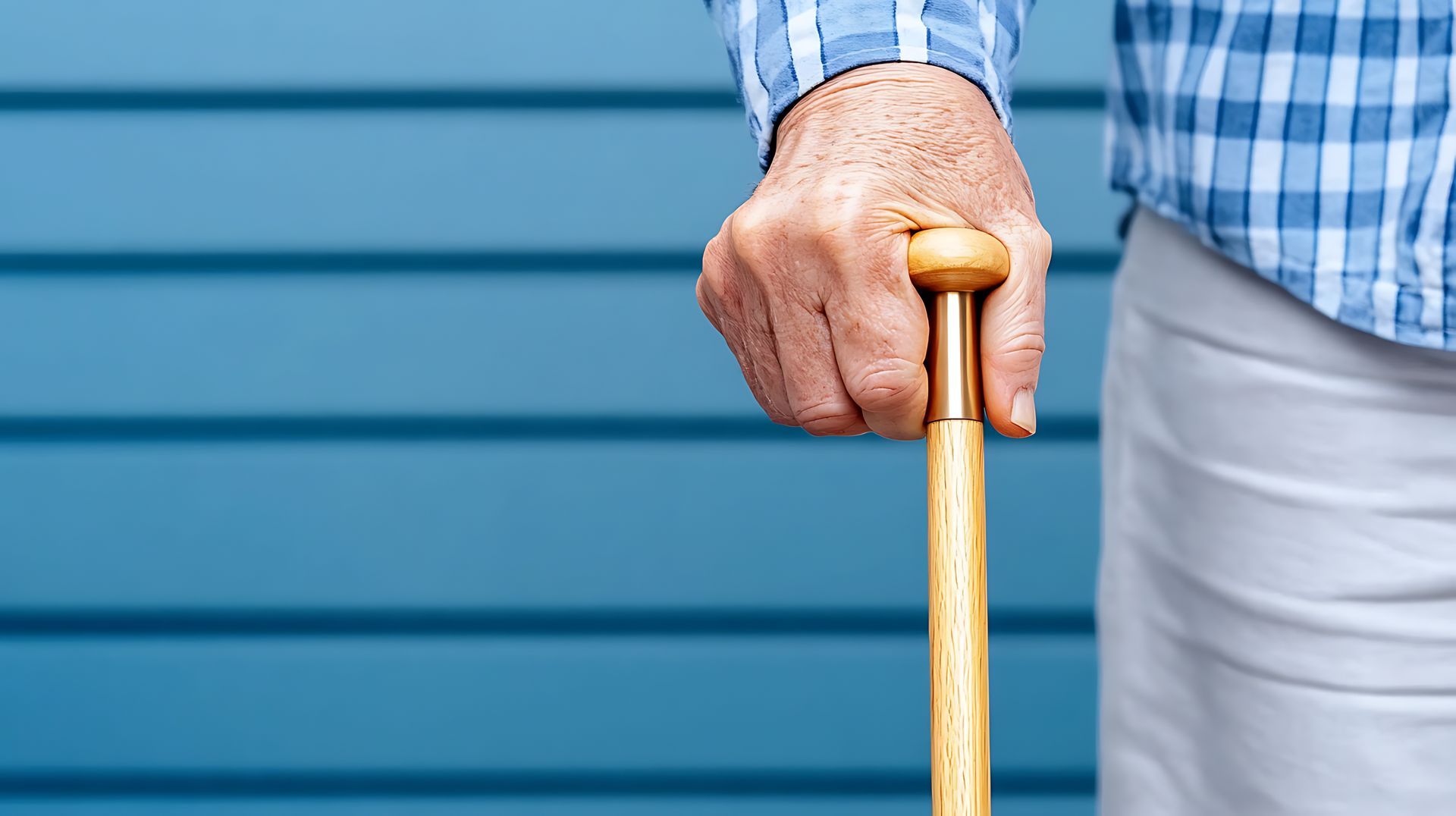 Close-up of a hand holding a wooden cane against a blue paneled background. Close-up of a hand holding a wooden cane against a blue paneled background.