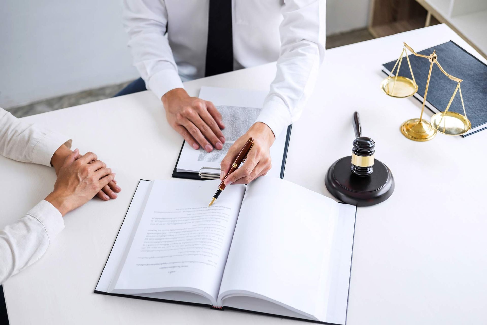 Lawyer advising client with legal papers, justice scales, and gavel on office desk during consult.