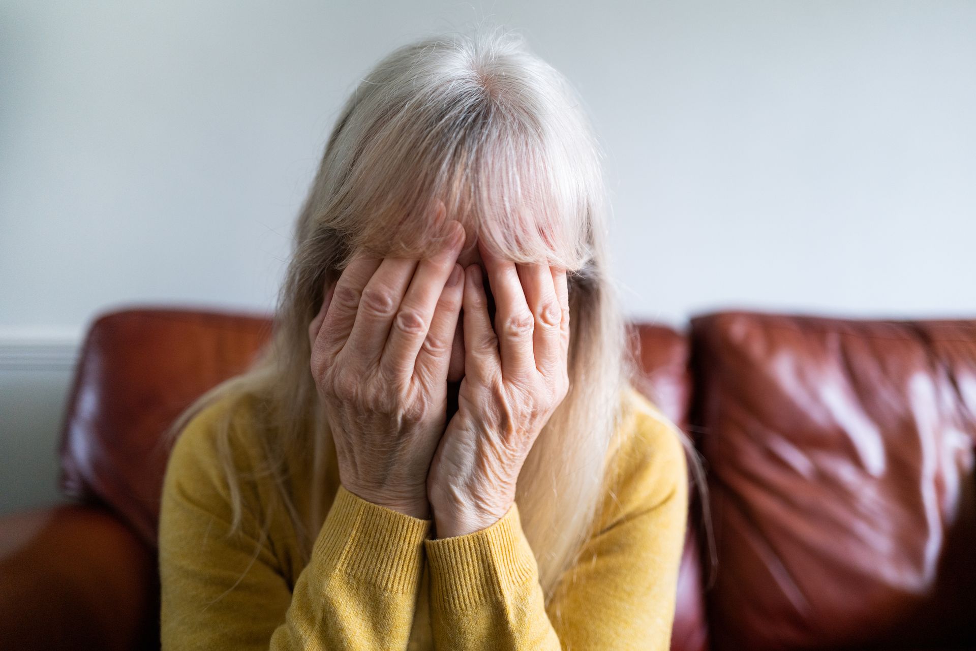 Sad-looking senior woman with hands over face at nursing home.