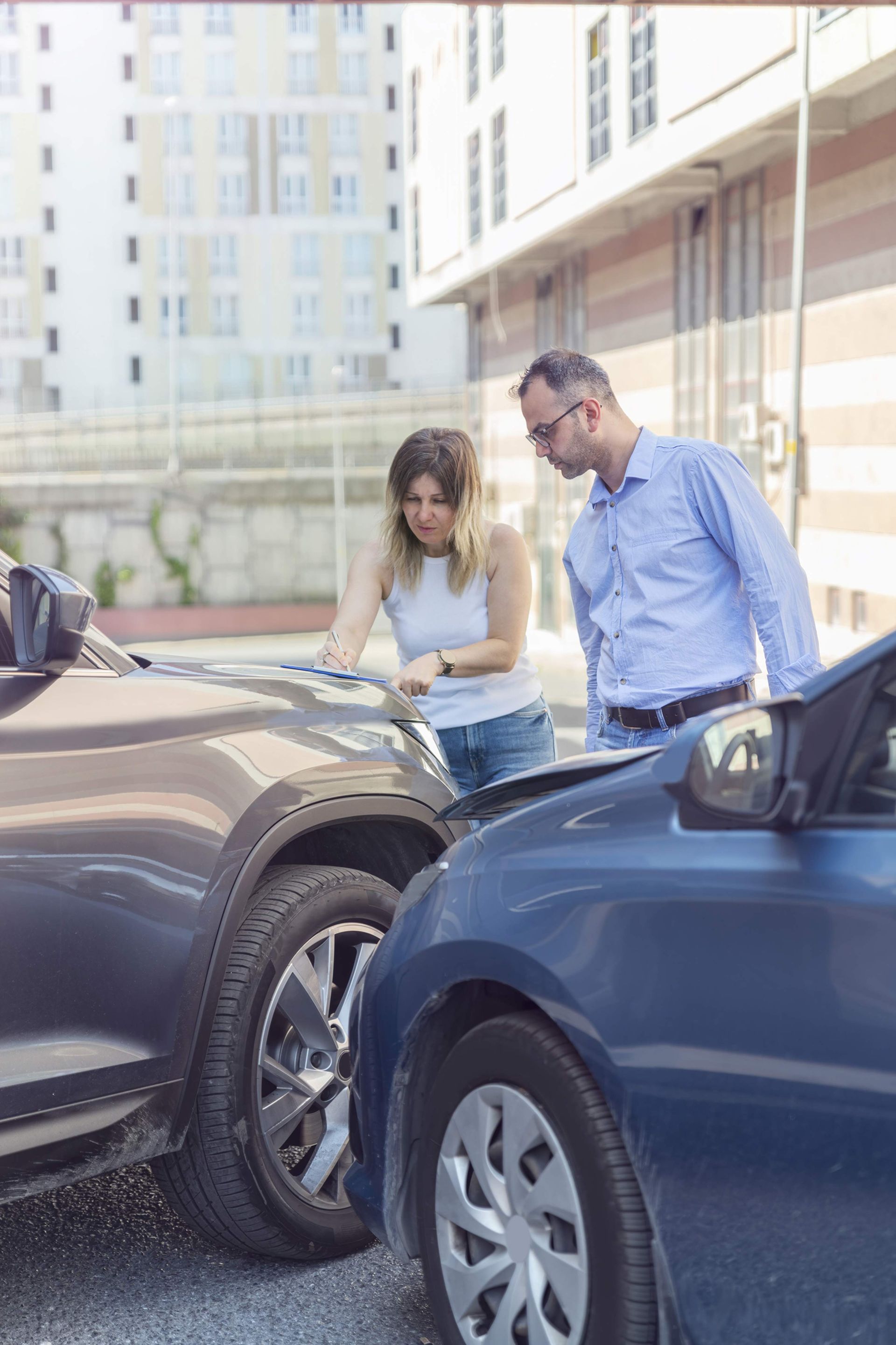 Two people inspecting damage to cars after a minor collision, exterior setting