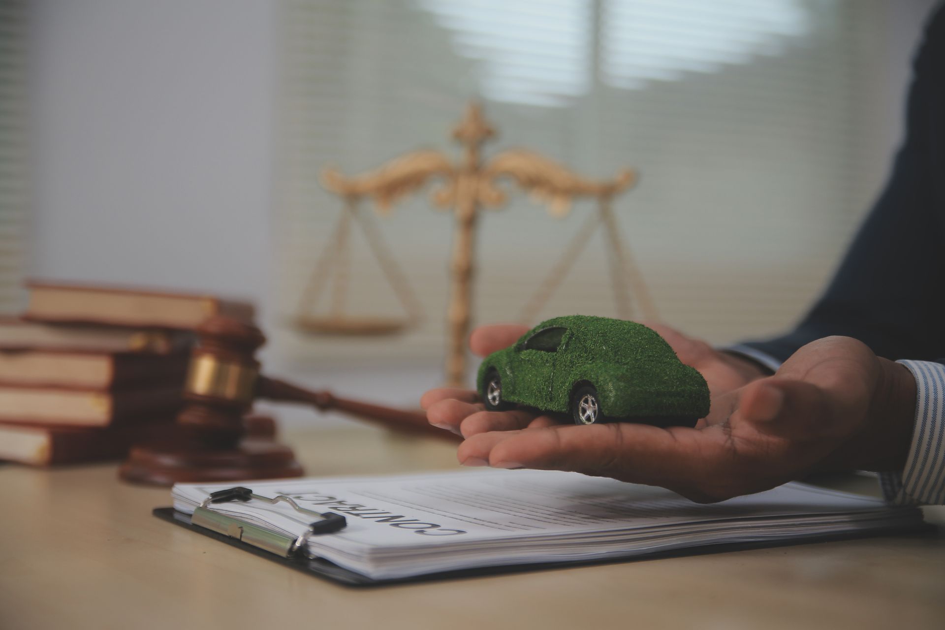Judge gavel, documents, and miniature green car in hand, symbolizing car accident attorney services.