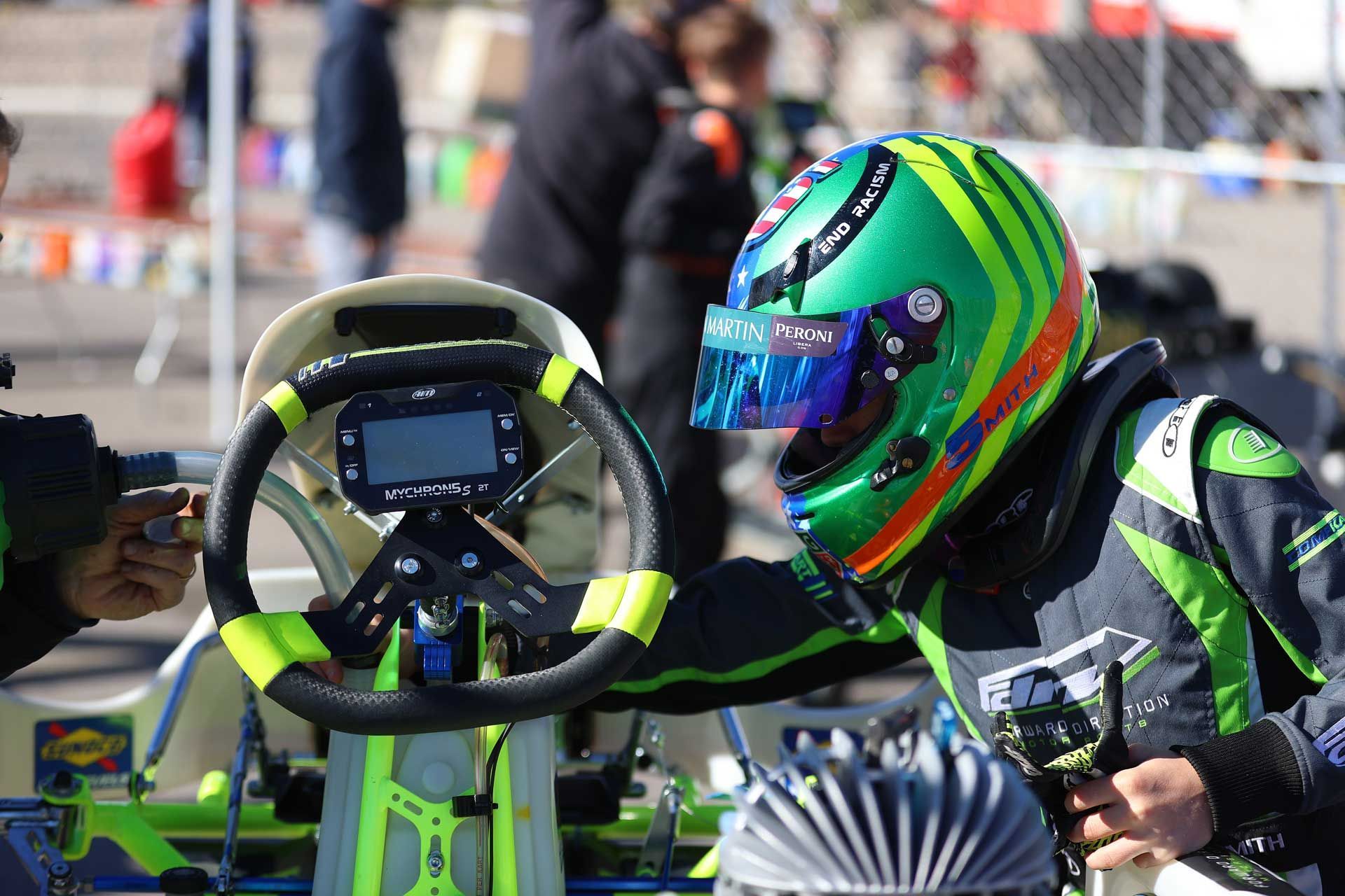 A man wearing a green helmet is sitting in a go kart.