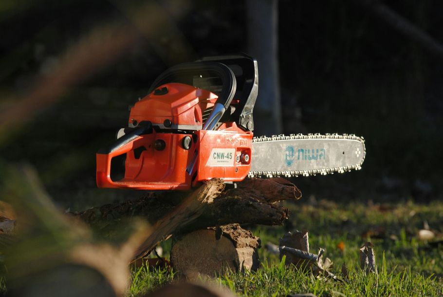 Orange Niwa CNW-45 gas chainsaw resting on a log in a grassy field.