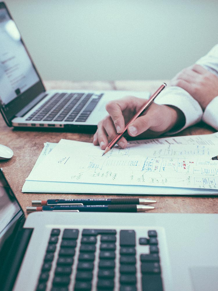 a person is writing on a piece of paper in front of a laptop computer .
