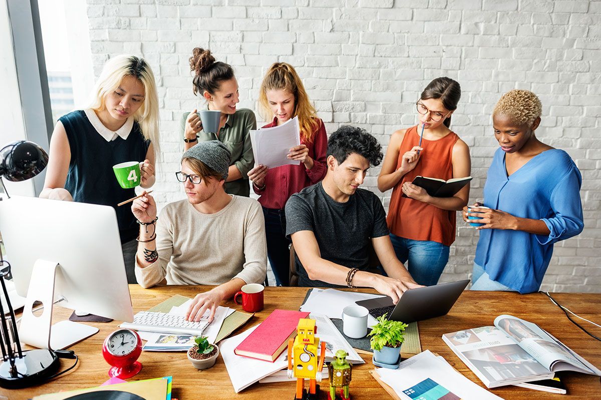 A group of people are standing around a table looking at a laptop.
